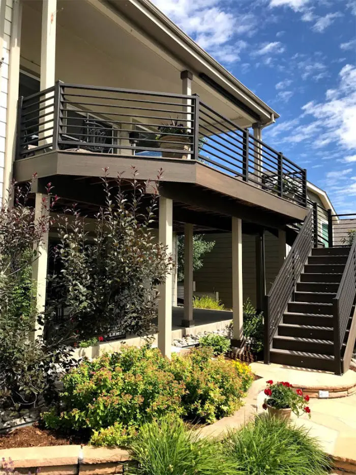 Raised deck with horizontal black railing and stairs above landscaped beds