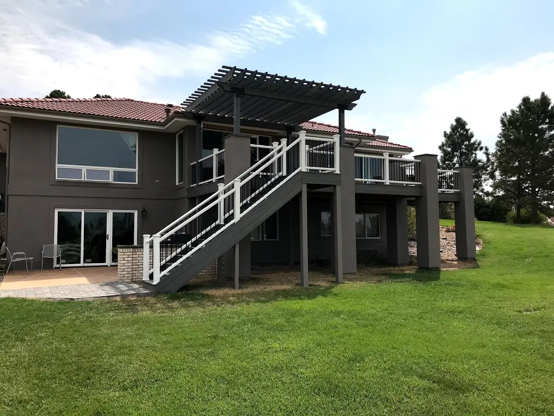 Two-story deck with a pergola and white-railed stairs down to the lawn