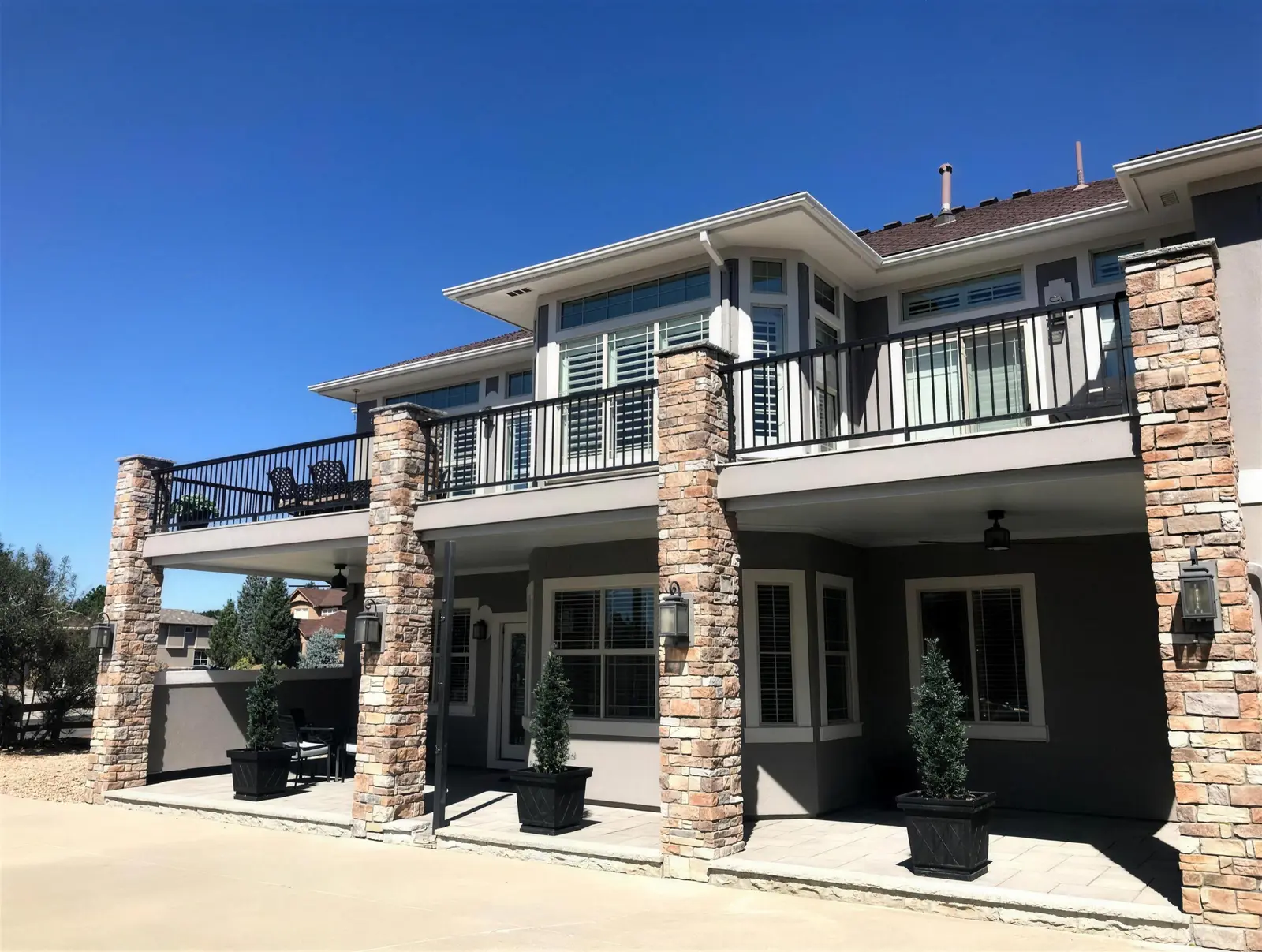 Two-story home with an upper deck, black metal railing and stacked stone columns over a covered patio