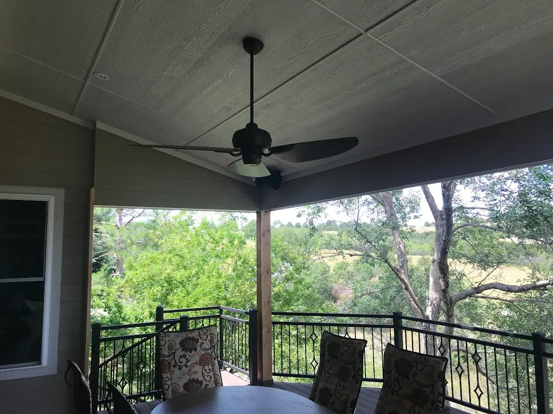Covered deck with a ceiling fan, black railing and seating overlooking trees